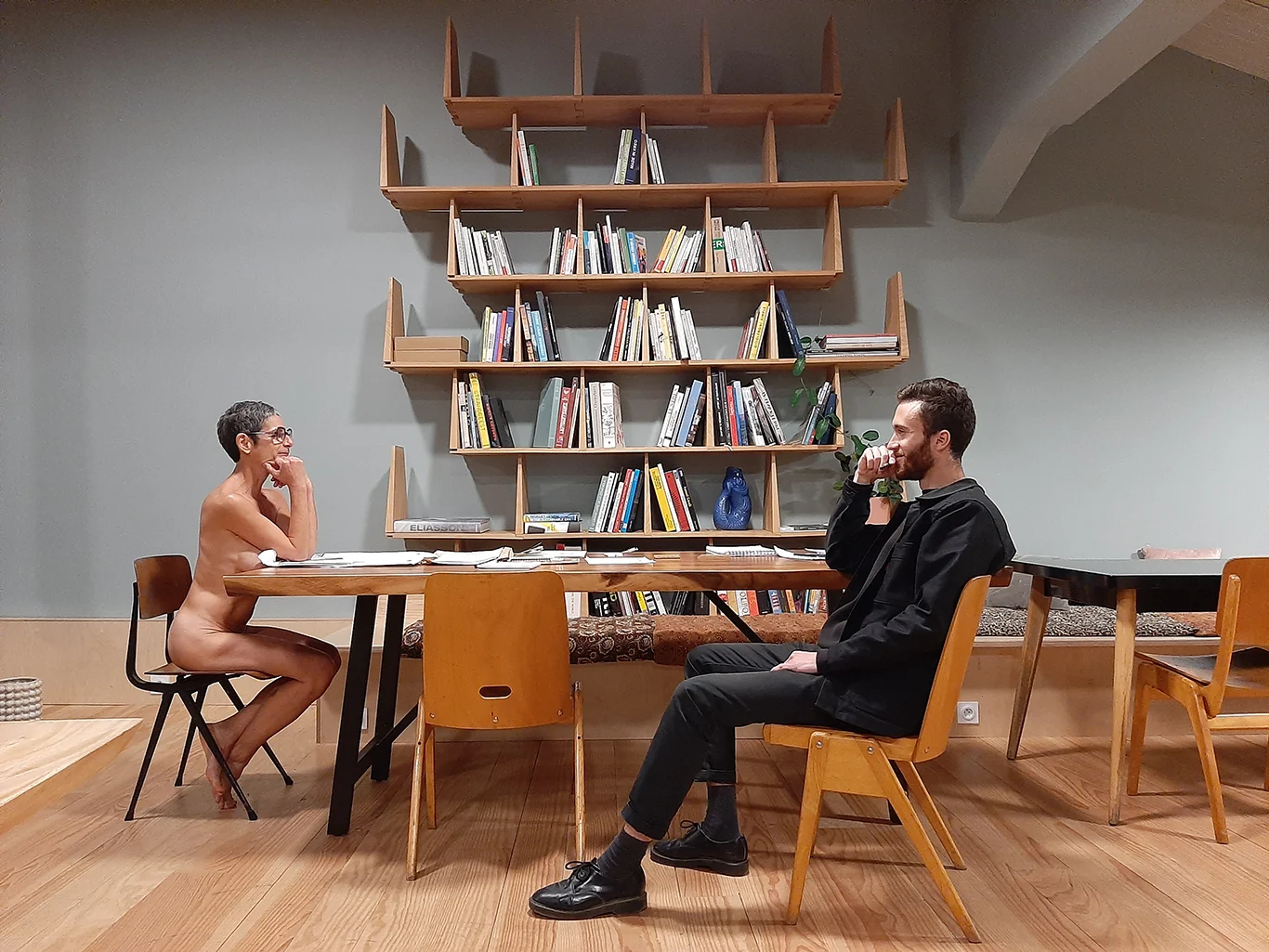 Gisèle Didi et Guillaume Bloget assis de part et d’autre d’une table, devant une bibliothèque.