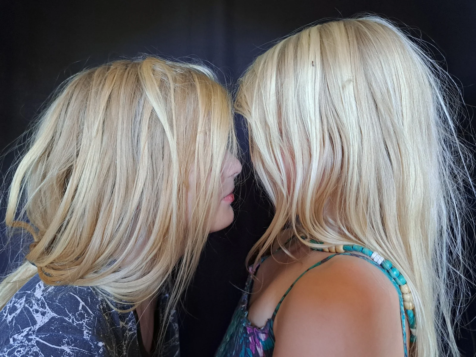 Deux femmes aux cheveux blonds se font face sur un fond sombre.